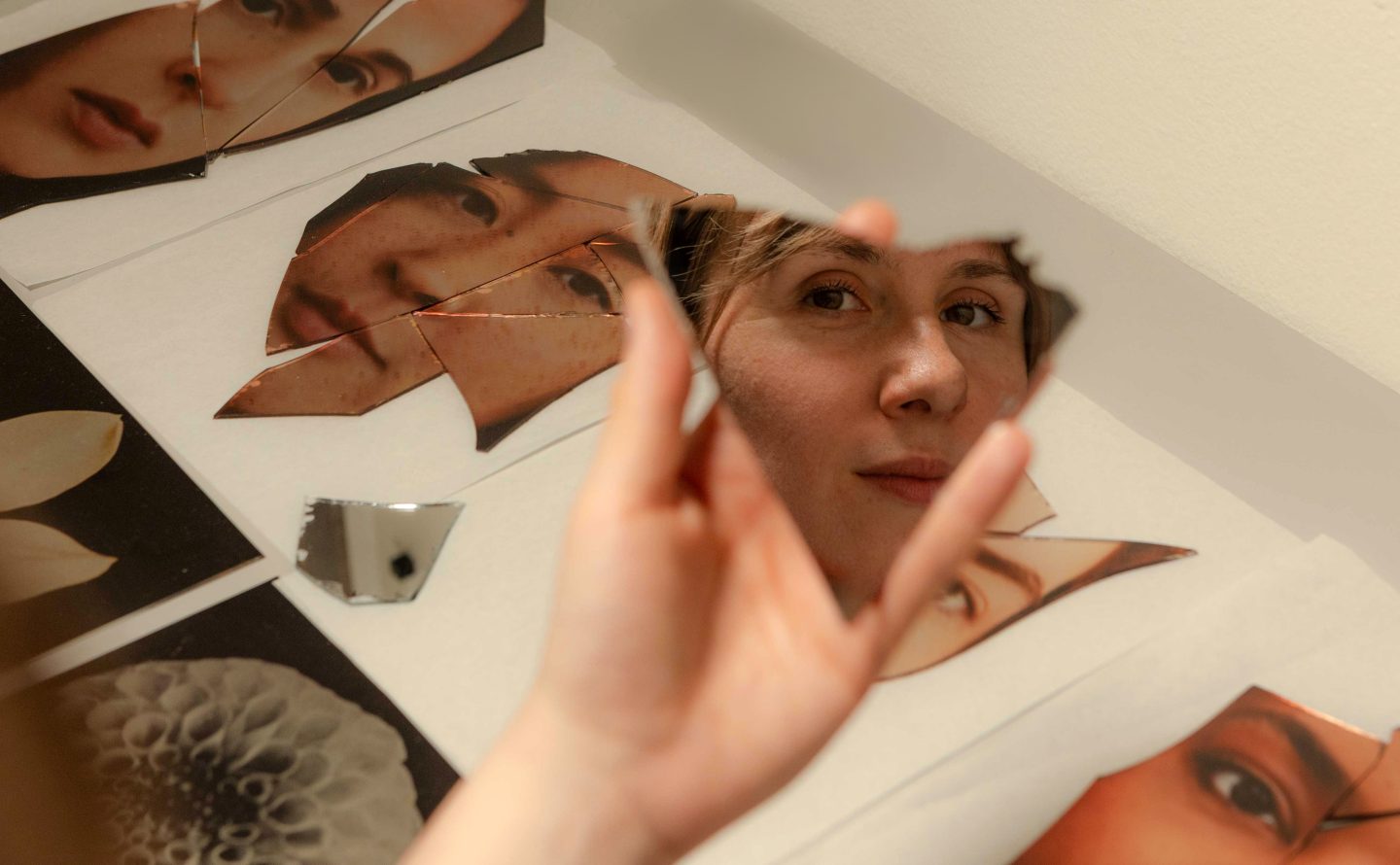 Abstract portrait in a photography and new media workshop showing a woman looking into a fragmented mirror piece with related printed photographs on a table